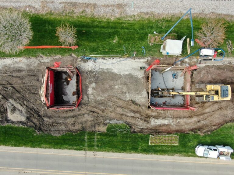Aerial view of a trenchless construction site with two excavation pits, equipment, and vehicles along a roadway.